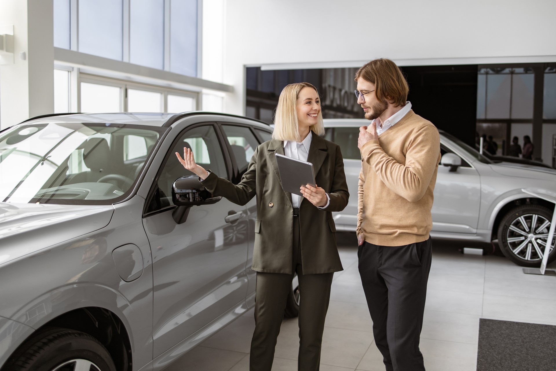 Confident saleswoman explaining all car features using tablet to handsome owner.