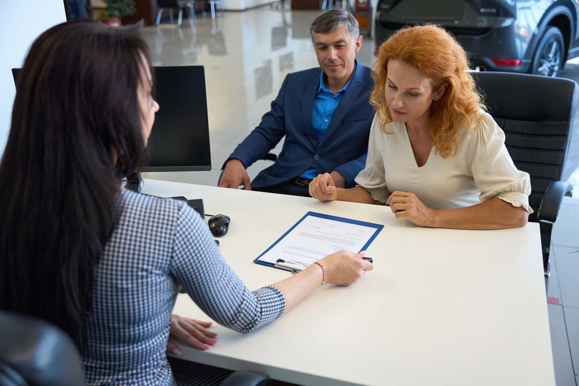 Customers chatting with car dealership manager at office desk