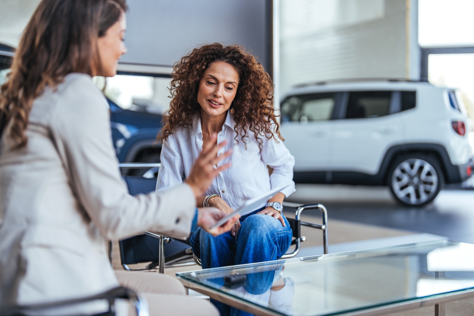 Smiling car saleswoman discussing a contract with a female customer.